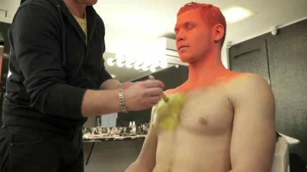 Мастер макияжа, покрывающий грудь человека ярко-желтого цвета — стоковое видео