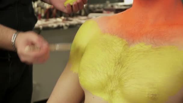 Arte maquillaje maestro que cubre los hombros de los hombres con color amarillo con el cepillo — Vídeo de stock