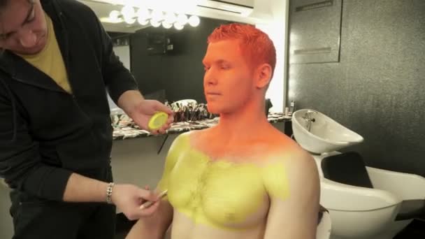 Makeup master täcker mans kropp med gul färg med penseln — Stockvideo