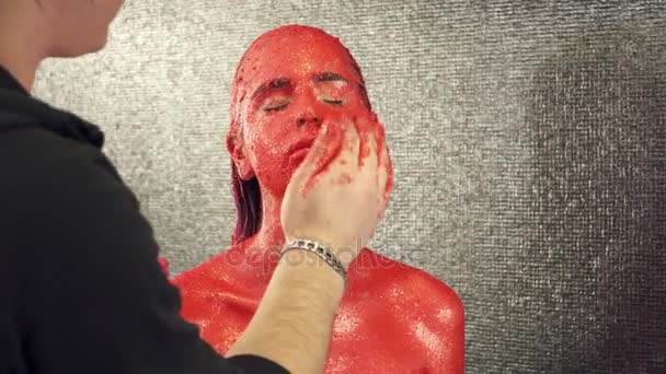 Maquilleuse couvrant le visage des filles avec de la peinture rouge vif dans le studio — Video