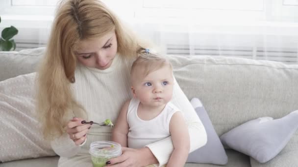 Молодая мать кормит своего маленького мальчика из тарелки — стоковое видео