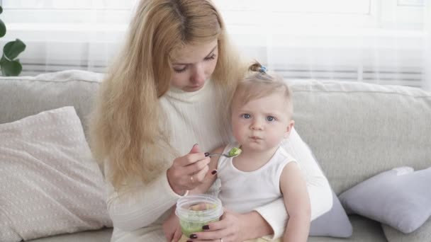 Молодая мать кормит своего маленького мальчика сидя на диване — стоковое видео