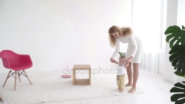 Madre ayudando a su pequeño hijo a caminar en la habitación — Vídeos de Stock