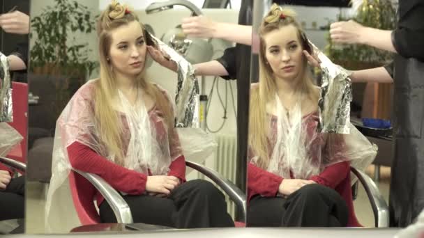 Парикмахер раскрашивает волосы молодых женщин перед зеркалом — стоковое видео