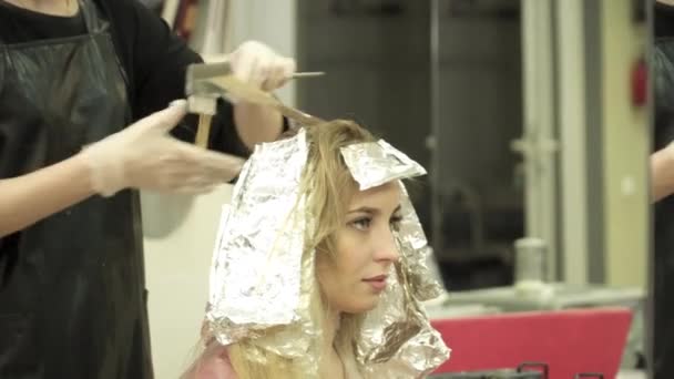 El estilista para colorear bandadas de cabello rubio en el salón de belleza — Vídeo de stock