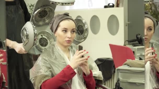 Женщина сушит волосы в машине для сушки волос в салоне — стоковое видео