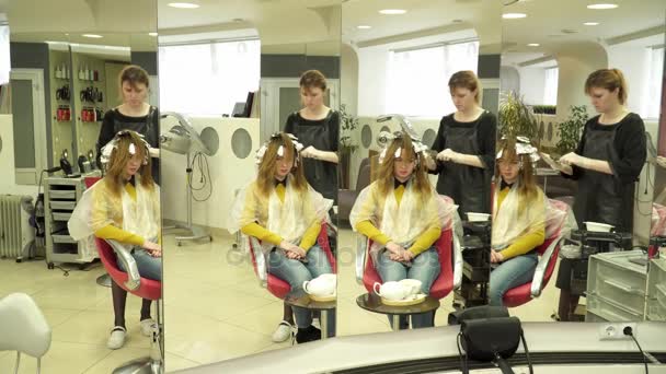 Парикмахер красил девушкам стаи волос перед зеркалом — стоковое видео