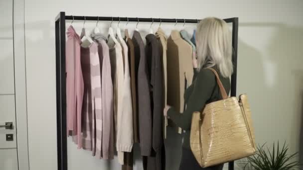 Молода блондинка в бутіку вибирає одяг, щоб купити . — стокове відео
