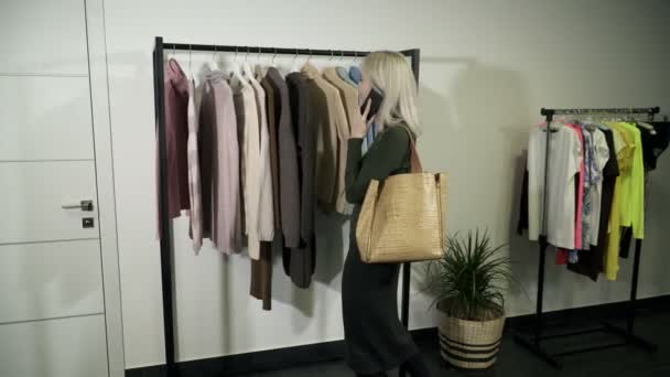 Ung kvinna i boutique att välja nya kläder till buyand talar i telefon — Stockvideo