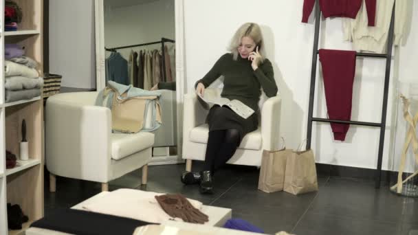 Jonge blonde vrouw lezen magazine en praten aan de telefoon bij boetiek — Stockvideo