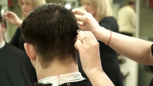 Hairdresser is making a haircut for a young man in salon — Stock Video