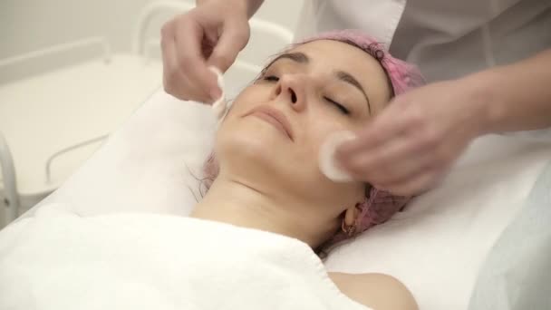 Косметолог розчищає жіноче обличчя ватним майданчиком — стокове відео