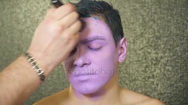 Makyaj sanatçısı kapsayan genç adamın yüzü ile bir boya fırçası ile