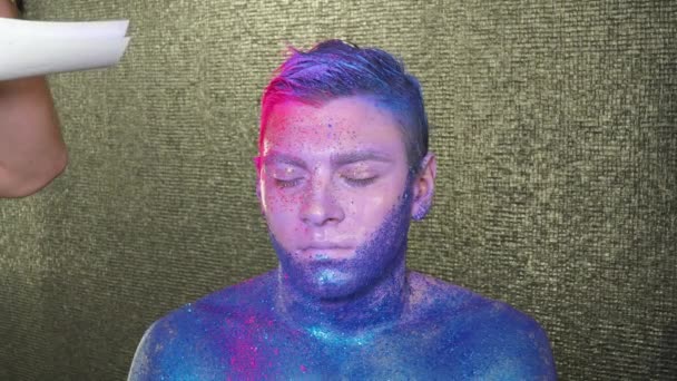 Макіяж художник покриває обличчя чоловіка рожевим порошком — стокове відео