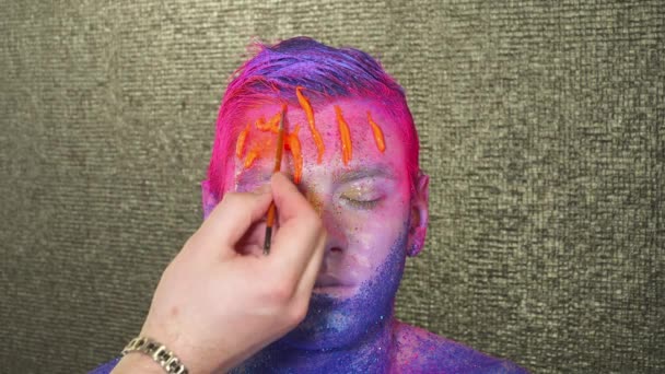 Body art maker oranje verf te gieten de mans gezicht — Stockvideo