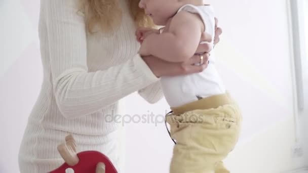Genç anne oğlunu tahta at oyuncağın üstüne oturmak için yardım — Stok video