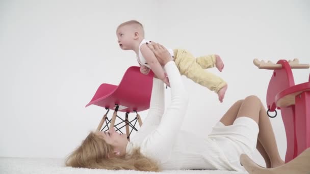 Joven madre jugando con su niño feliz tirado en el suelo y vomitándolo — Vídeos de Stock