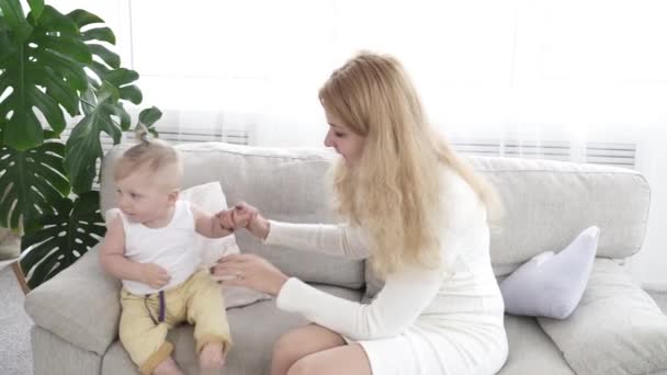 Молодая мать помогает своему маленькому сыну ходить по дивану — стоковое видео