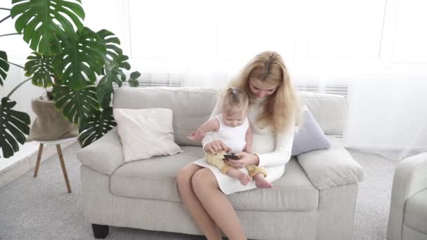 Молодая красивая мама показывает что-то на смартфоне своего маленького ребенка — стоковое видео