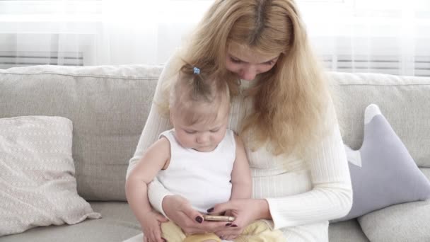 Молода мати щось показує на смартфоні свою маленьку дитину — стокове відео
