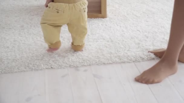 Mãe ajudando seu pequeno filho a andar no quarto, close-up — Vídeo de Stock