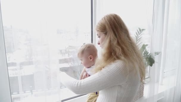 Junge Mutter blickt mit ihrem Sohn an den Händen aus dem Fenster — Stockvideo