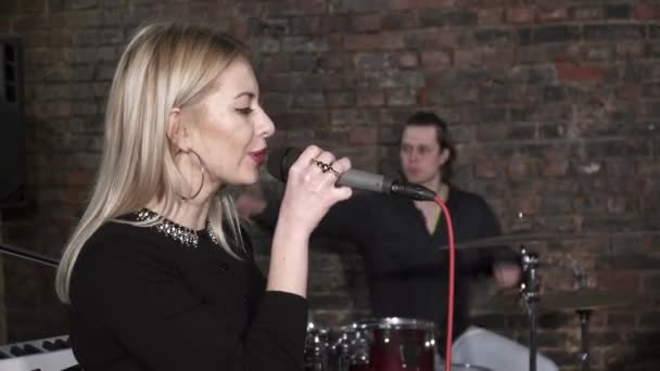 Młoda kobieta śpiewa do mikrofonu z mężczyzną, grając na perkusji na tle — Wideo stockowe