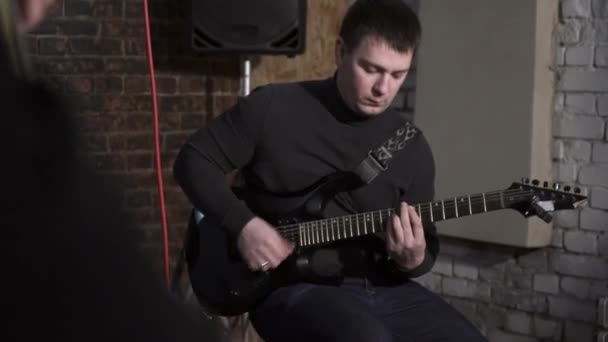 Молодой человек сидит и играет на гитаре в студии — стоковое видео