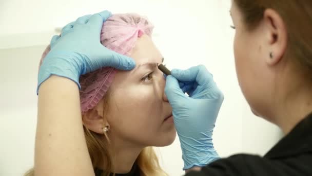Cosmetologist que prepara a mulher nova para a composição permanente das sobrancelhas closeup — Vídeo de Stock