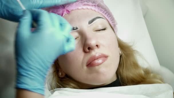 Schoonheidsspecialiste is het toepassen van lokale verdoving voordat de wenkbrauw permanente make-up procedure closeup — Stockvideo