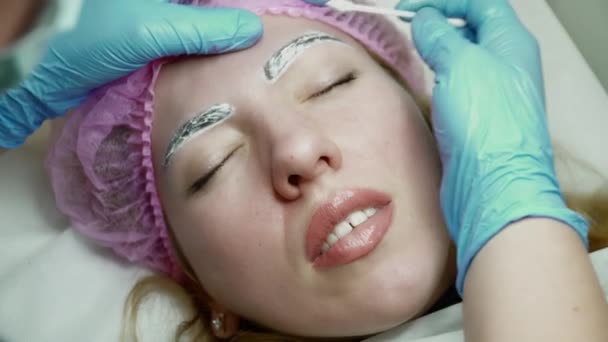 Schoonheidsspecialiste is het toepassen van lokale verdoving voordat de wenkbrauw permanente make-up procedure closeup — Stockvideo