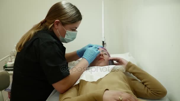 Ung kvinna prata i telefon samtidigt ha ett permanent makeup förfarande — Stockvideo