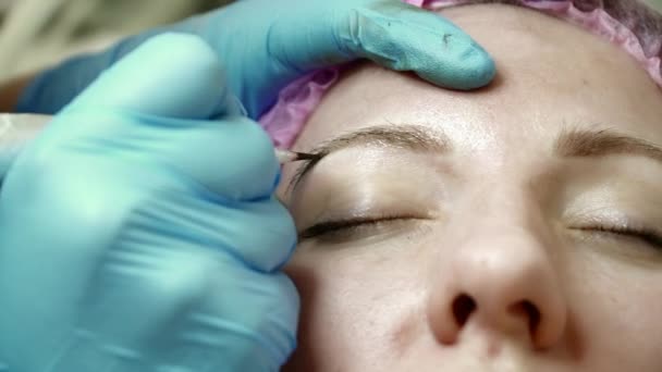 Closeup αισθητικός κάνει ένα φρύδι μόνιμη μακιγιάζ για μια γυναίκα στο σαλόνι — Αρχείο Βίντεο