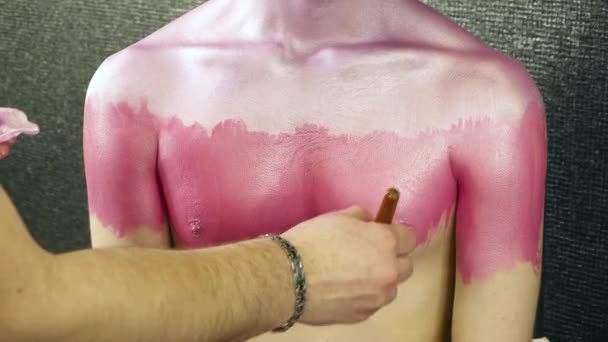 Makeupartist som täcker ung mans hals med en rosa färg — Stockvideo