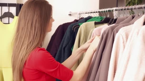 Mujer joven eligiendo ropa nueva en la tienda — Vídeos de Stock