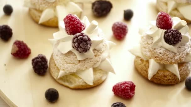 Beautiful tasty eclairs with the cream and berries on the wooden surface — Stock Video