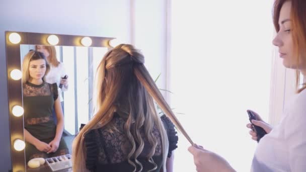 Peluquería creando un peinado para una mujer joven frente al espejo — Vídeos de Stock
