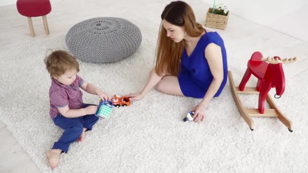 Молодая мать играет со своим маленьким сыном с машинами на ковре замедленной съемки — стоковое видео