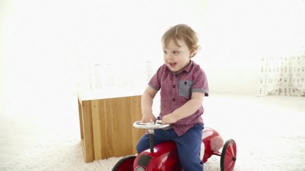 Маленький мальчик за рулем игрушечной машины в комнате — стоковое видео