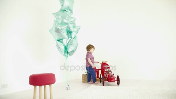 Niño pequeño conduciendo un coche de juguete alrededor de la habitación — Vídeo de stock