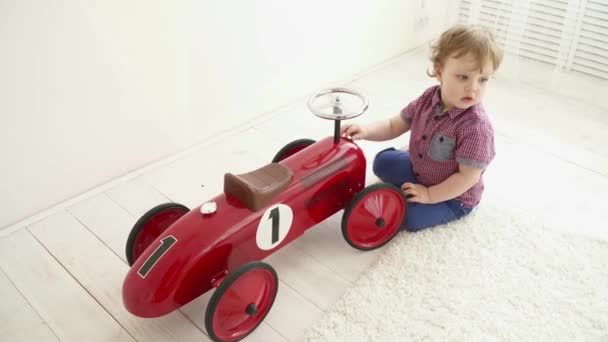 Pequeño niño jugando con un gran coche de juguete en la habitación — Vídeos de Stock