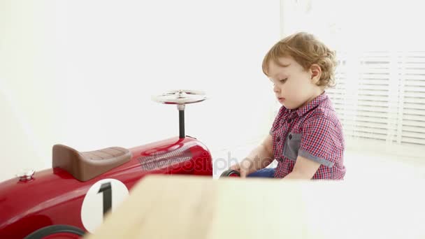 明るい部屋で大きなおもちゃの車で遊ぶ小さな男の子 — ストック動画