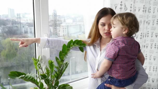 Молода мати дивиться у вікно зі своїм маленьким сином — стокове відео