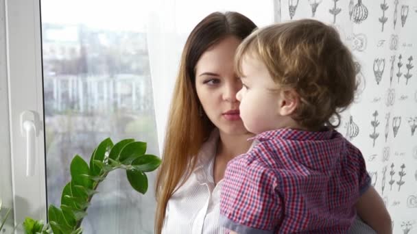 Молодая мать смотрит в окно со своим маленьким сыном крупным планом замедленной съемки — стоковое видео
