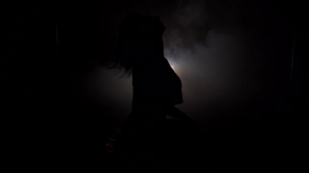 Jonge slanke dames silhouet in de rok dansen in de donkere kamer-closeup — Stockvideo