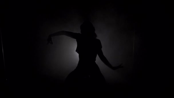 Young slim womans silhouette in the skirt dancing in the dark room with smoke closeup — Stock Video