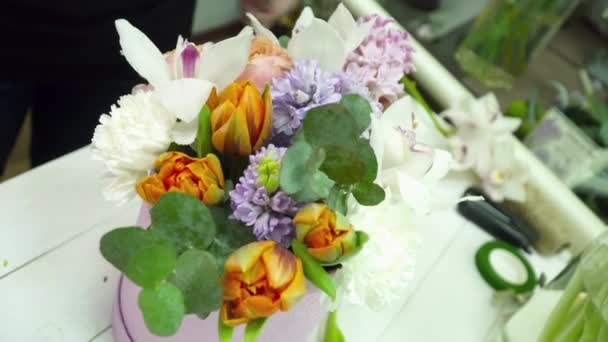 Floristería creando un hermoso ramo en la caja en la mesa de madera en la tienda — Vídeos de Stock