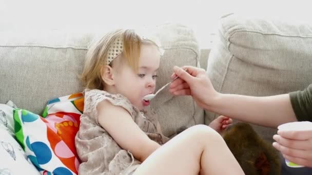 Молодая мать кормит свою дочь на диване крупным планом — стоковое видео