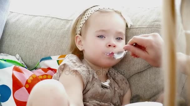 Young mother feeding her daughter with a spoon on the couch — Stock Video