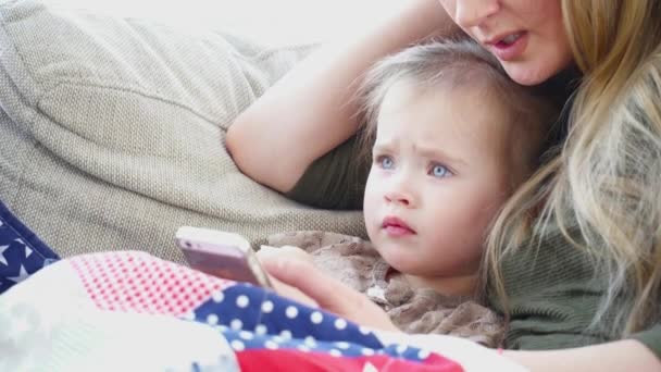 Mère utilisant le téléphone portable avec sa petite fille allongée sur le canapé 